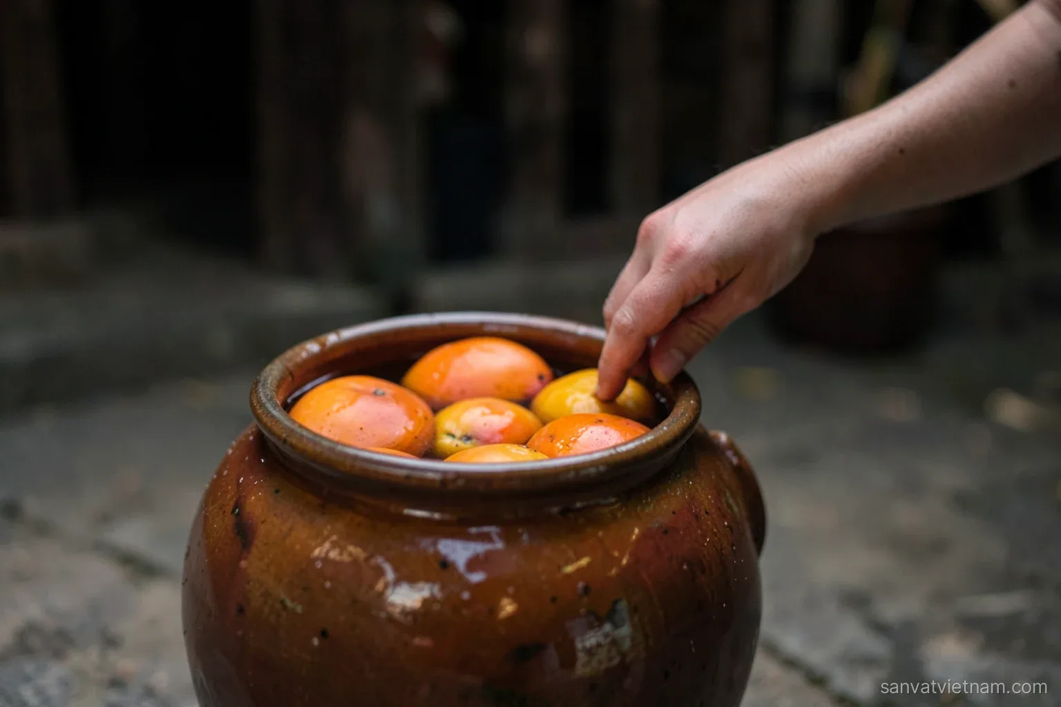 Close-up of orange persimmons floating in a glazed clay jar of water in a dim village courtyard, a hand reaching in, soft autumn light